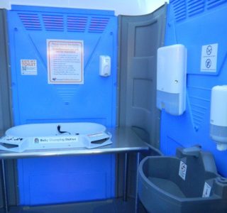 Interior view of a portable toilet equipped with baby changing station and hygiene facilities.