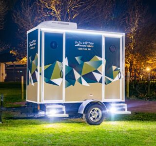 Illuminated mobile bathroom trailer at night in a park setting