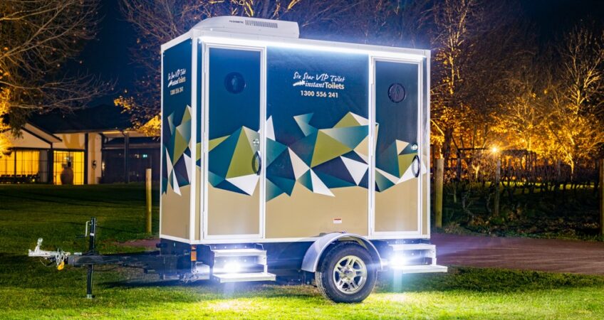 Illuminated mobile bathroom trailer at night in a park setting
