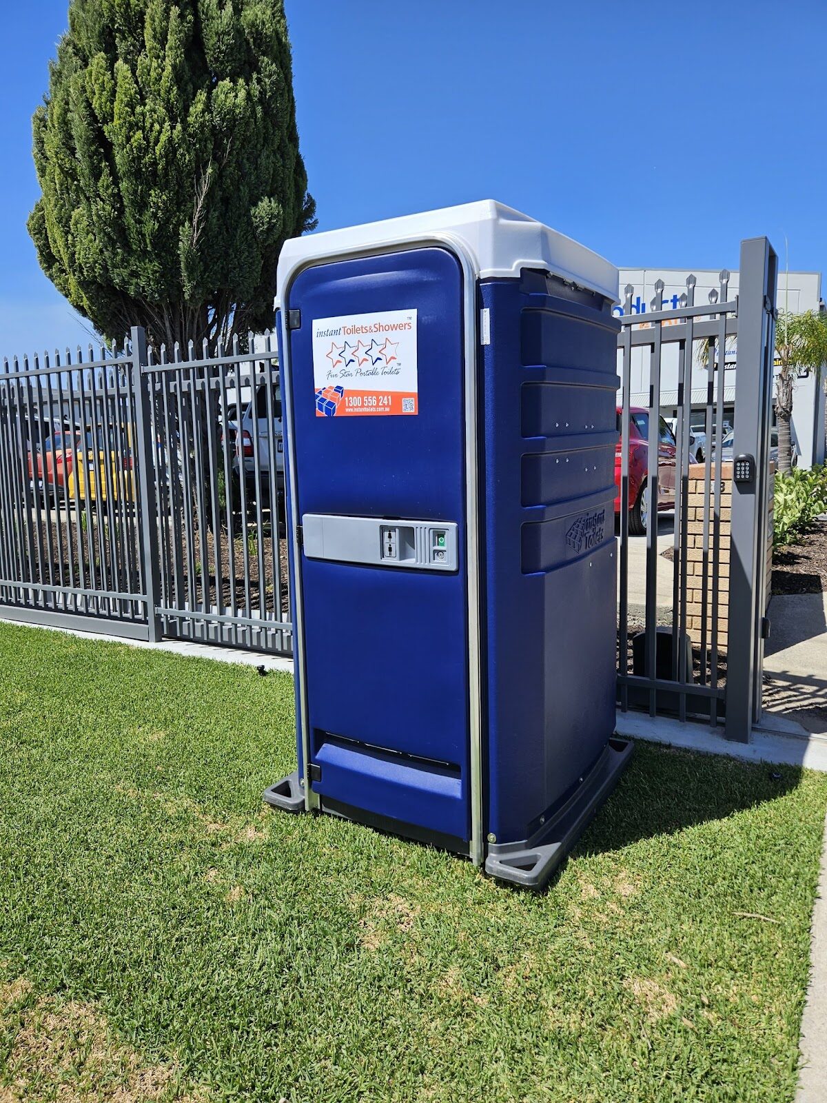 Blue Five Star Event Chemical Toilet with LED Lighting next to a fence and tree in a sunny outdoor setting.