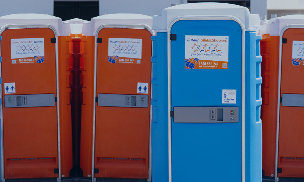 Instant Toilets & Showers portable toilet units lined up on site, featuring all-gender signage and company branding