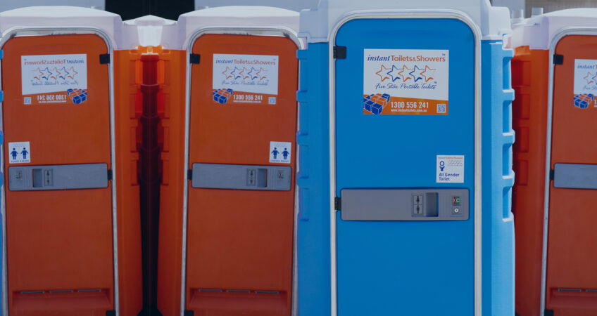 Instant Toilets & Showers portable toilet units lined up on site, featuring all-gender signage and company branding