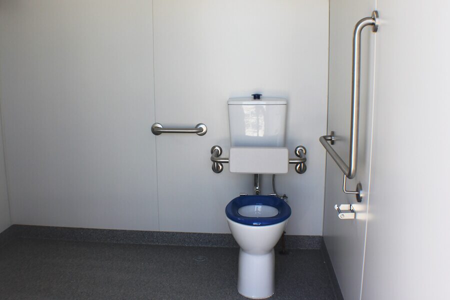 Interior of an accessible bathroom with safety handrails, a blue toilet seat, and grey flooring.