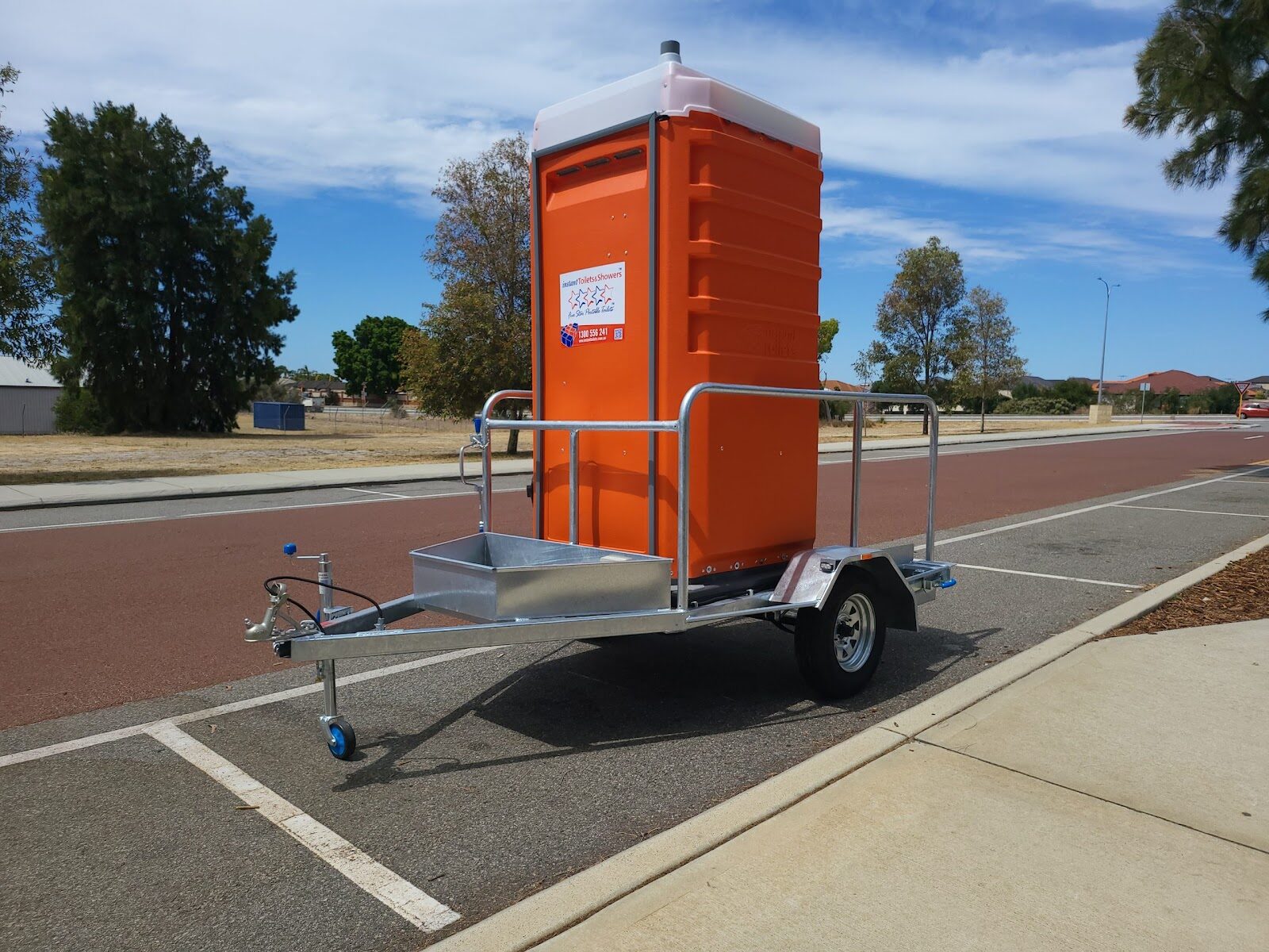 Orange Five Star Mobile Event Toilet on a trailer parked by a roadside.