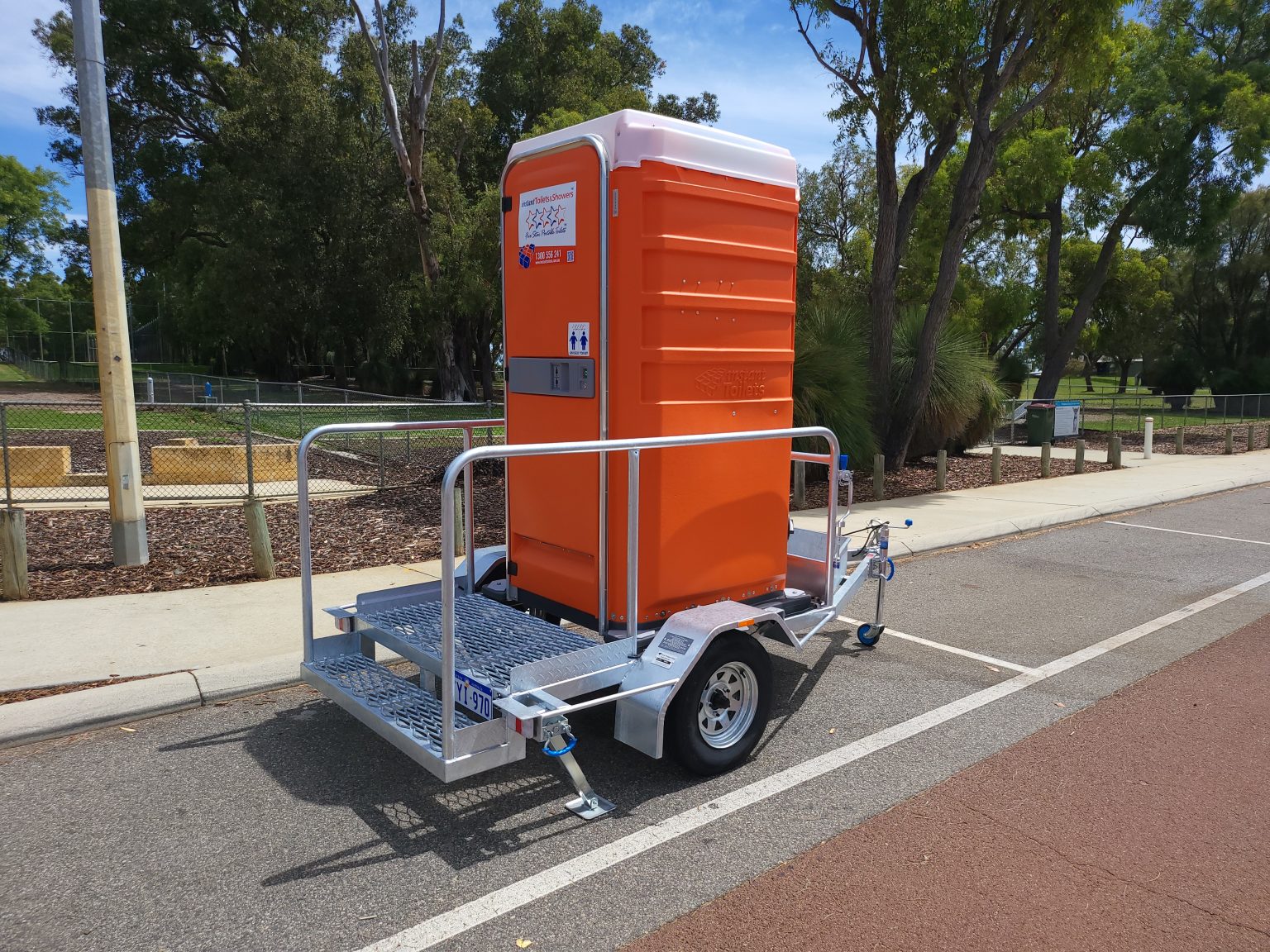 Portable orange restroom unit mounted on a trailer for easy transport.