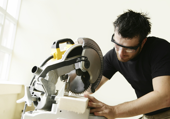 Man using a circular saw to cut wood, wearing protective glasses in a workshop.