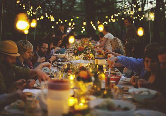 Outdoor dinner party with people seated at a long table under string lights.