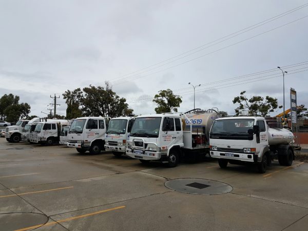 Row of septic trucks using for portable toilet services parked in an outdoor lot on a cloudy day.