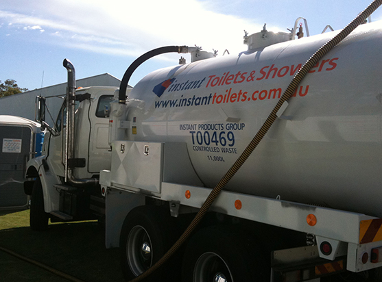 Septic truck using for portable toilet services with hose attached, parked near portable toilets.