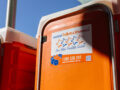 Close-up of a Five Star Event Chemical Portable Toilet from Instant Toilets & Showers, showing the company logo, five-star branding, contact number, and website URL on the door