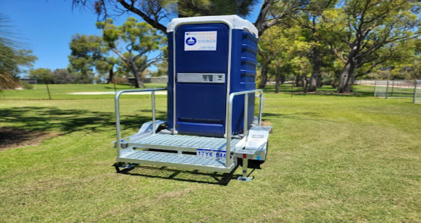 Portable shower unit mounted on a trailer in a sunny park setting.