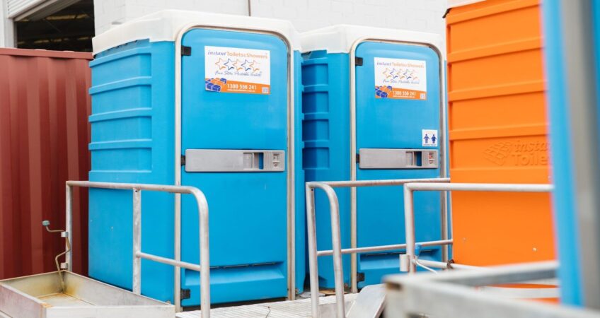 Portable blue toilets with railings and washing stations set up in an industrial area.