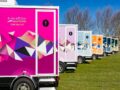 Row of colorful luxury portable toilet trailers with geometric designs parked on a grassy area
